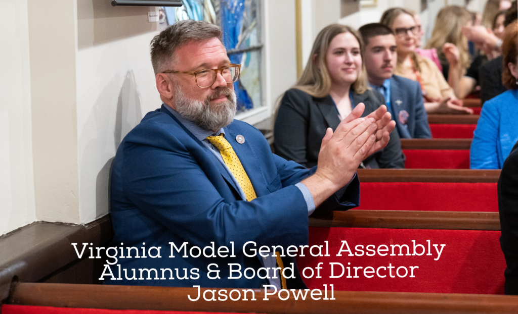 A bearded man wearing glasses, a blue suit, and a yellow tie clapping while seated in a red pew, with overlaid text reading 'Virginia Model General Assembly Alumnus & Board of Director Jason Powell'.