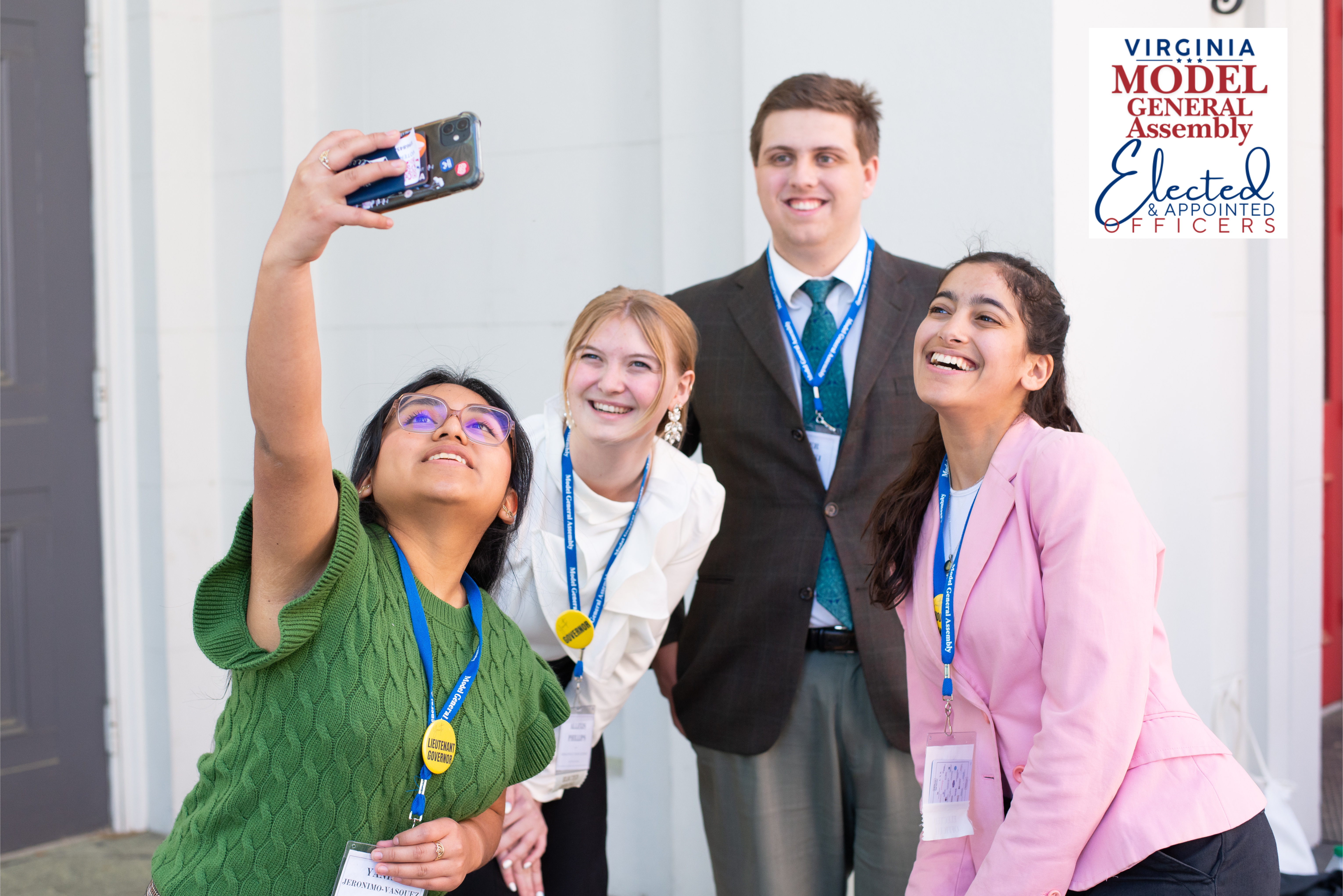Three smiling young adults wearing event lanyards taking a group selfie together, featuring the Virginia Model General Assembly Elected and Appointed Officers logo.