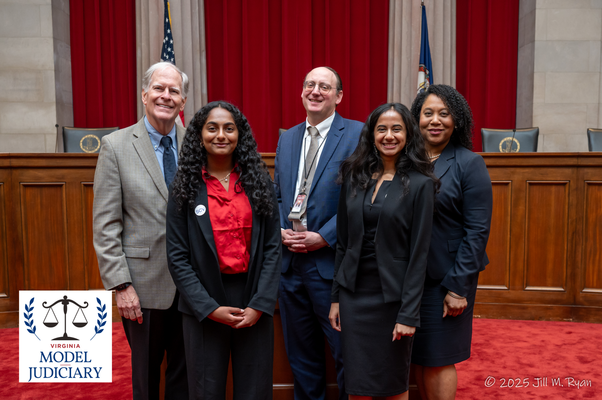 A group photo of five smiling individuals in professional attire posing in front of a wooden courtroom bench and red curtains, featuring the Virginia Model Judiciary logo and a 2025 Jill M. Ryan copyright.